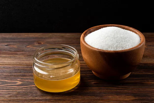 sugar in a wooden bowl and honey in a glass jar.