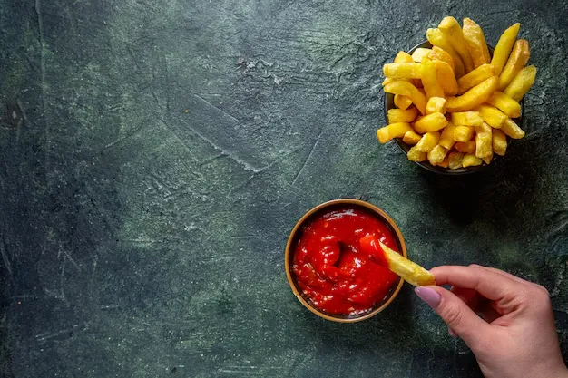 tomato ketchup placed with potato fries on a black surface.