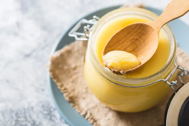 ghee in a glass jar with wooden spoon.